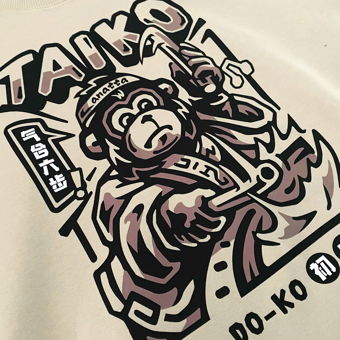 Taiko - a close-up of the design of a monkey dressed in traditional Japanese clothing playing a taiko drum, printed on the front of a khaki sweatshirt -2