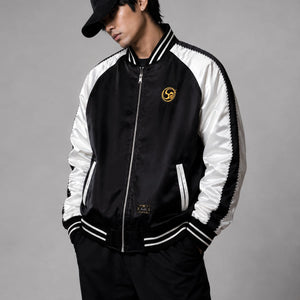 A model wearing the Raijin’s Wrath Japanese satin jacket, front view showing the black and white color-blocked design and embroidered chest logo