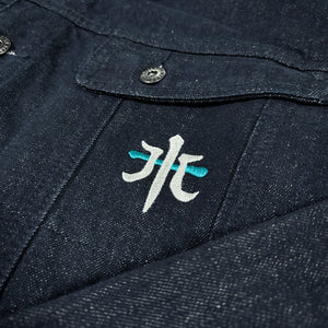 Close-up of the Rogue Wave denim jacket showing the embroidered chest symbol and textured indigo denim.