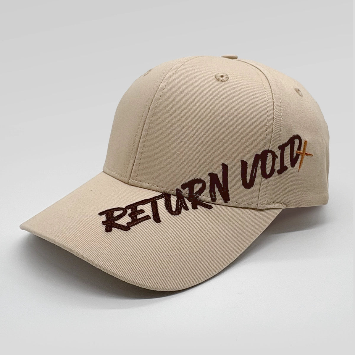 A beige baseball cap with 'RETURN VOID' embroidered across the front in dark brown and orange lettering, set against a plain light gray background.