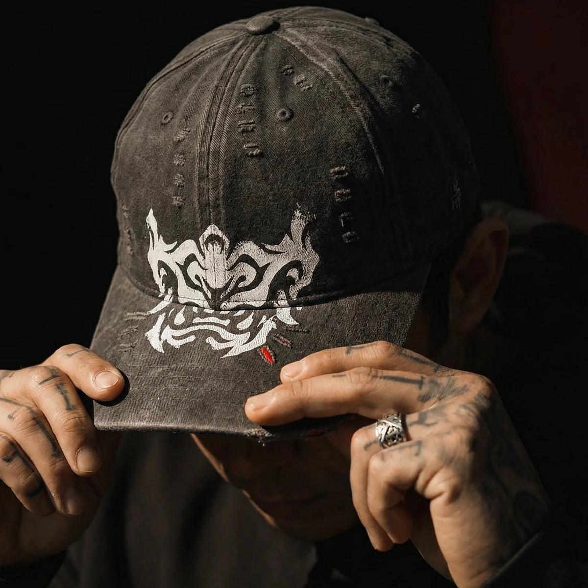 Person holding a black cap with white hannya graphic design against a dark background  - Anatta Streetwear