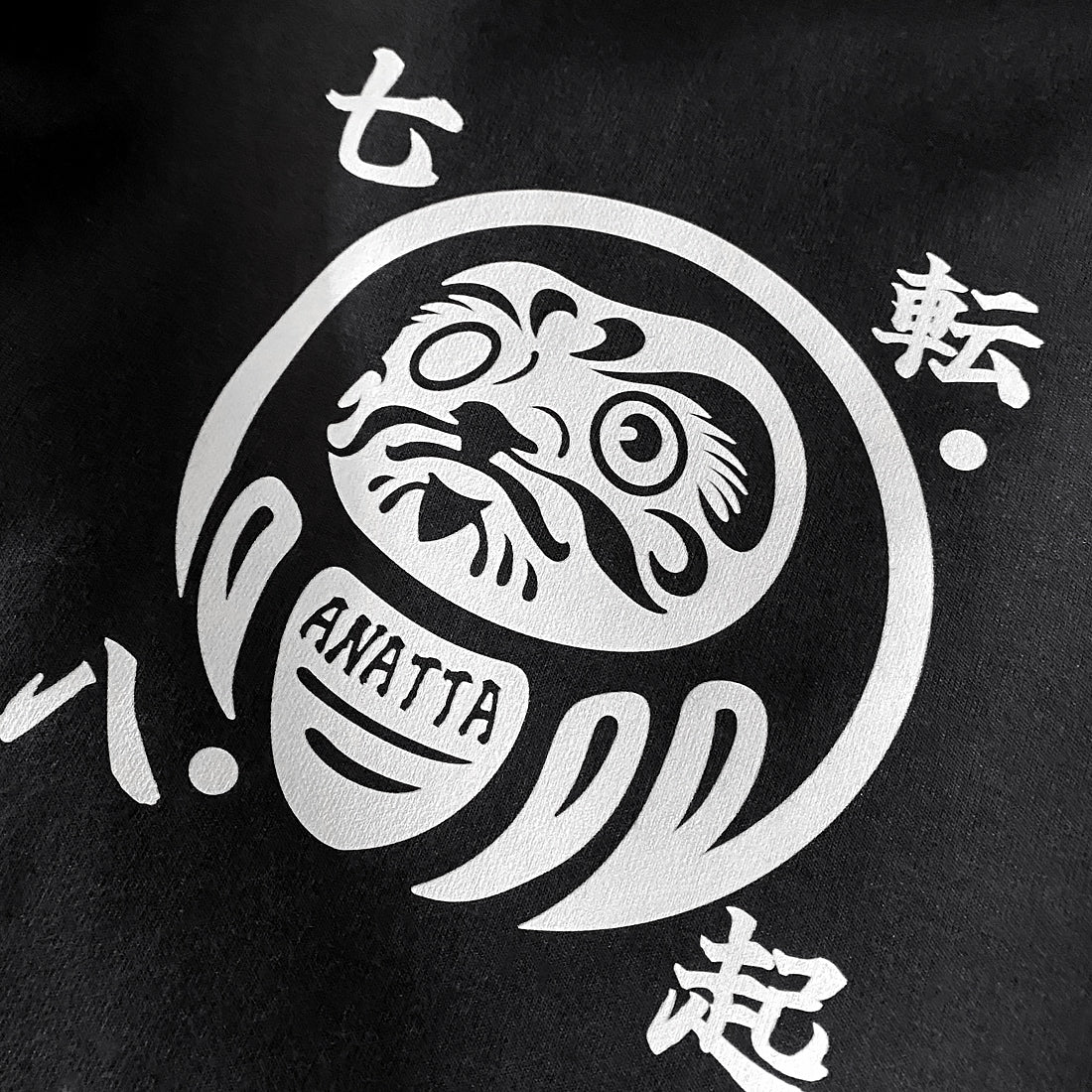 a close-up of a graphic design of a Japanese daruma doll, printed on the left of a Japanese style black shorts-Anatta Streetwear