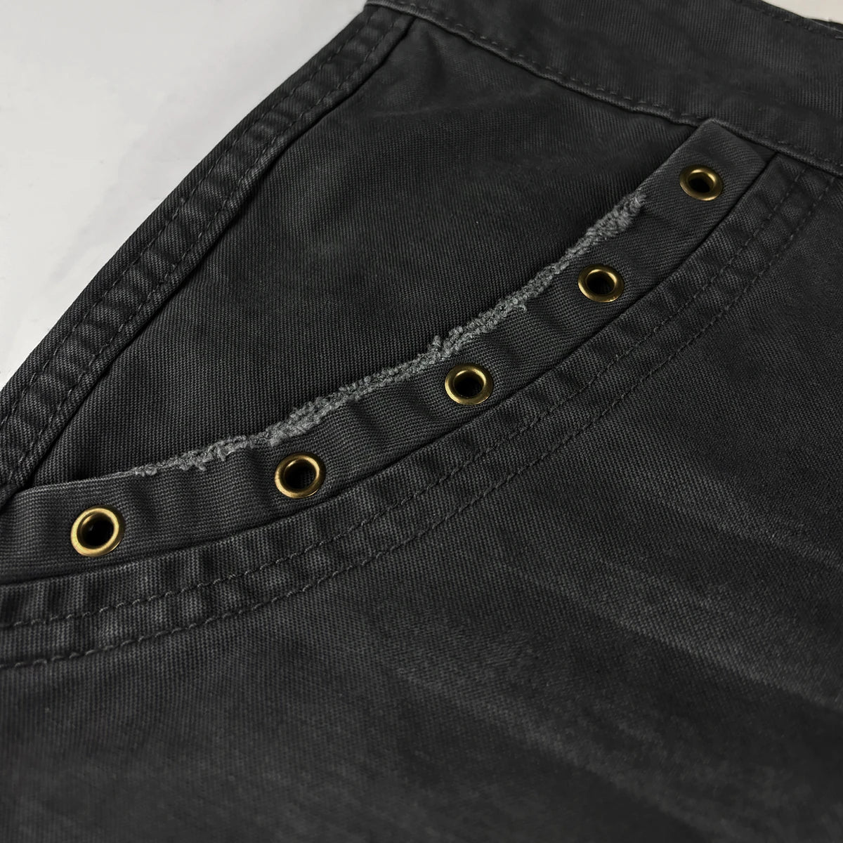 Close-up of black pants with gold buttons and stitching details - Anatta Streetwear