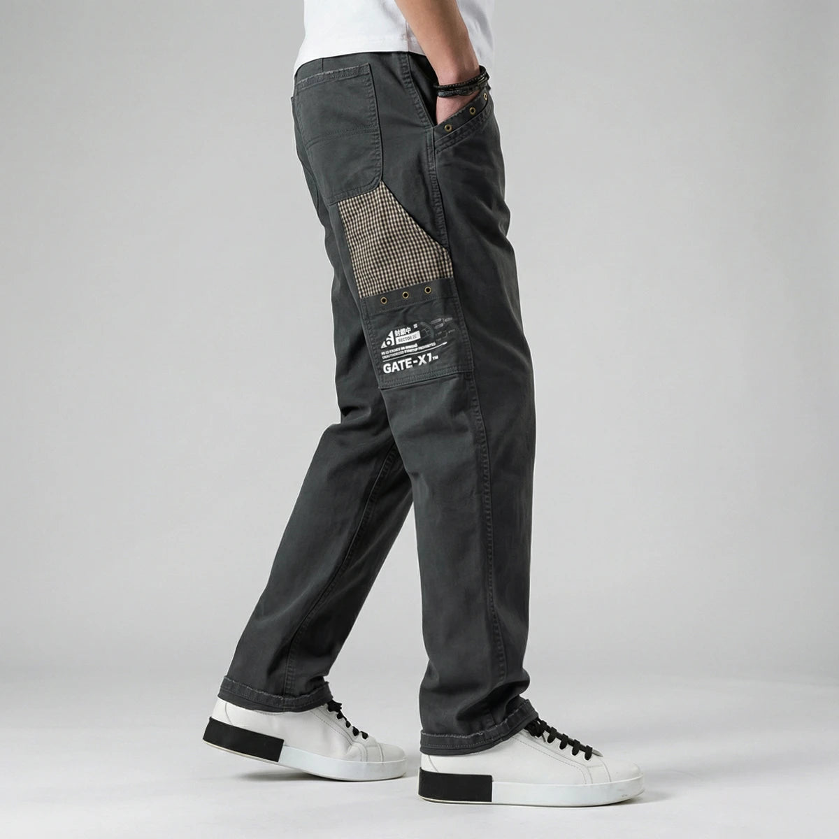 model wearing dark gray cargo pants with patches on a light gray background - Anatta Streetwear