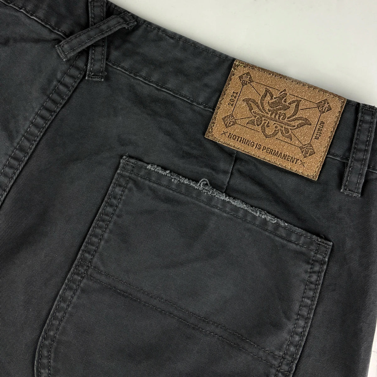 Close-up of dark gray pants with a brown leather label on a light gray background