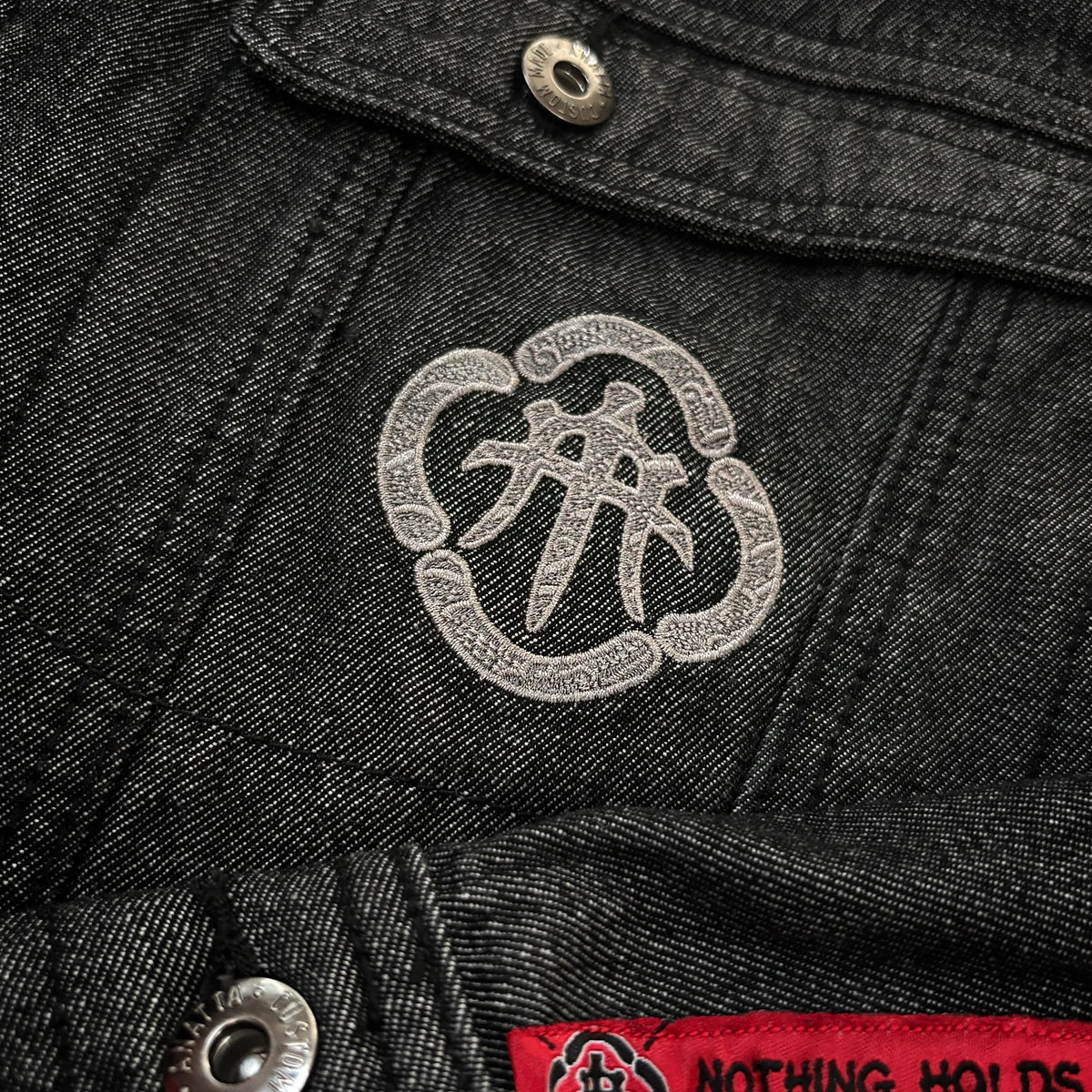 Close-up of embroidered Japanese chest emblem on the Fenikkusu dark grey denim jacket