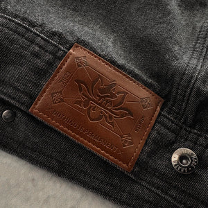 Close-up of the brown leather brand patch and metal hardware on the Fenikkusu dark grey Japanese denim jacket