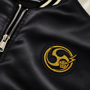 Close-up of the Raijin’s Wrath Japanese satin jacket, showing the gold embroidered chest logo and lustrous black satin fabric