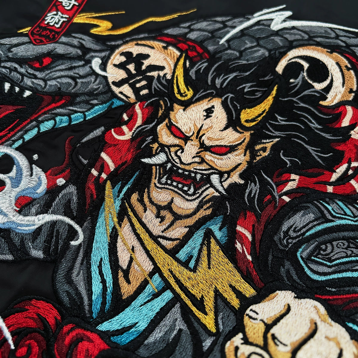 Close-up of the Raijin’s Wrath Japanese satin jacket embroidery, featuring Raijin, a serpent, thunder drums, lightning, and waves