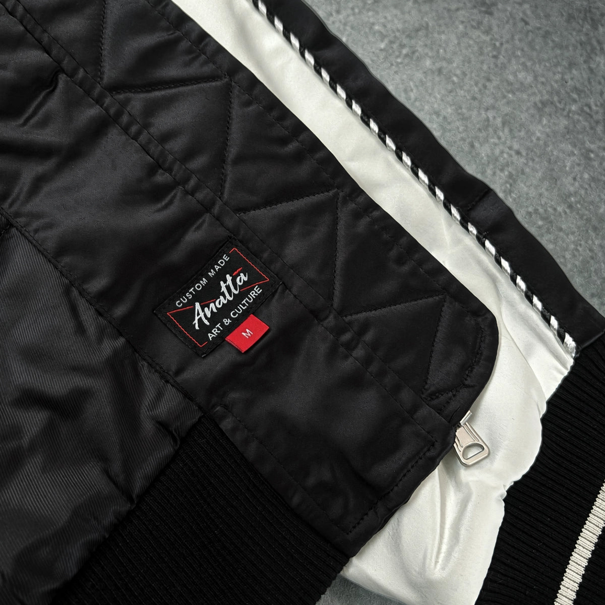 Close-up of the Raijin’s Wrath Japanese satin jacket interior, showing the quilted lining, inner pocket, zipper, and Anatta woven label
