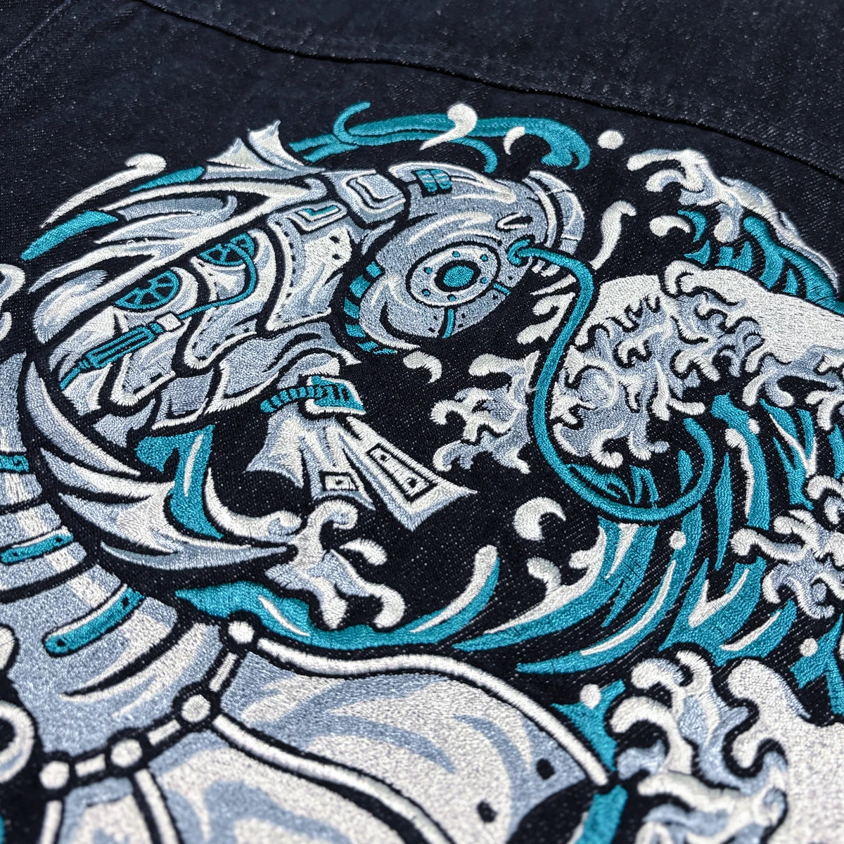 Close-up of the Rogue Wave denim jacket showing high-density Japanese wave embroidery in white and teal.