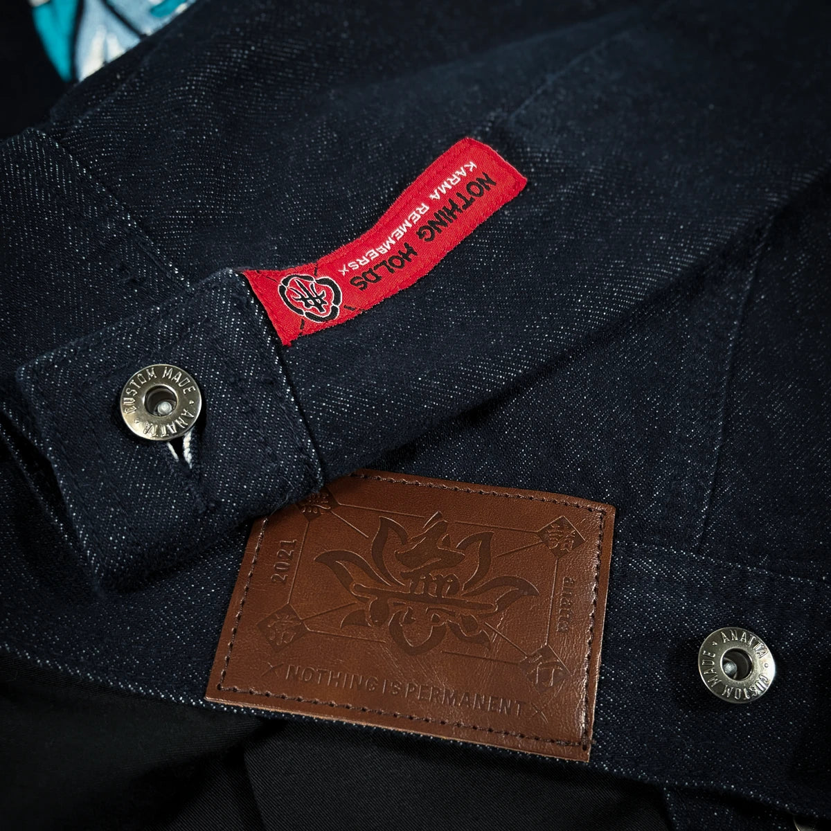 Close-up of the Rogue Wave denim jacket showing the red woven label, brown leather patch, metal buttons, and textured indigo denim.