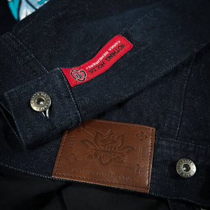 Close-up of the Rogue Wave denim jacket showing the red woven label, brown leather patch, metal buttons, and textured indigo denim.