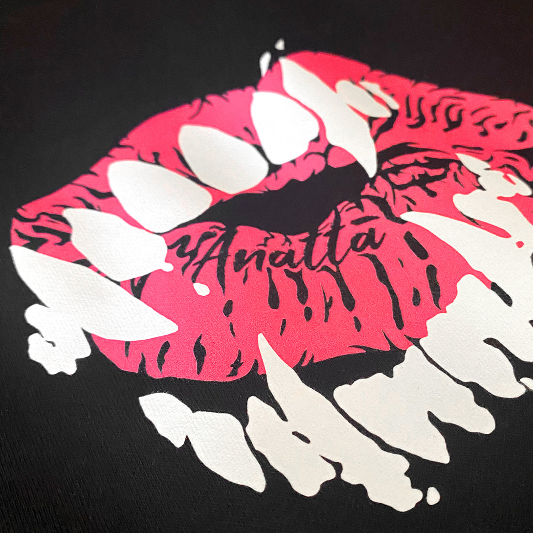 Chimei-teki - a close-up of a design combining red lips with devilish teeth, printed on the left chest of a black sweatshirt